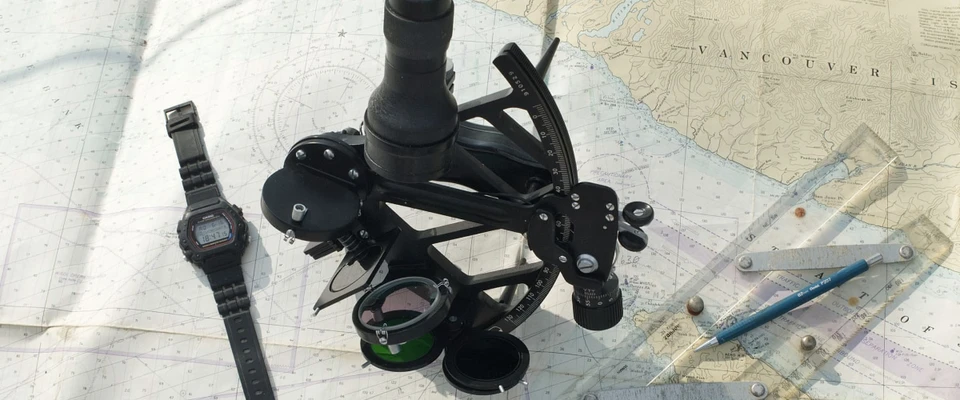 Sextant and wristwatch resting on a nautical chart with plotting tools.