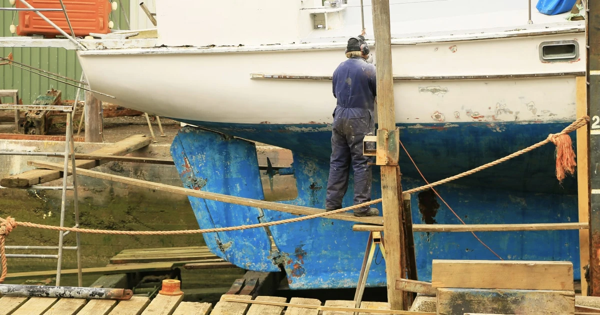 Sailboat hauled out of the water with a worker beside its hull.