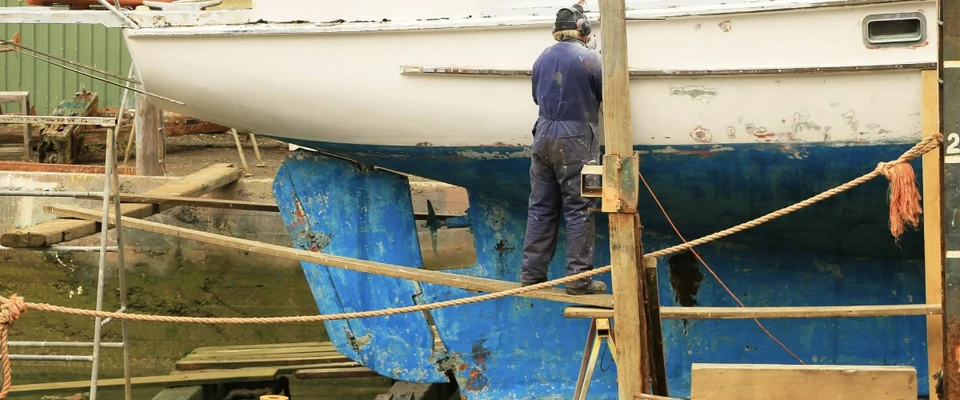 Sailboat hauled out of the water with a worker beside its hull.