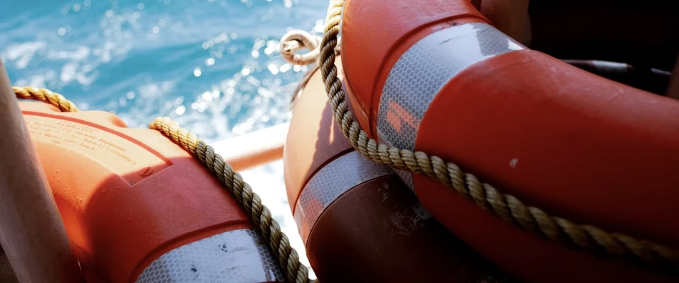 Orange lifebuoy with reflective bands on a boat, sea in the background.