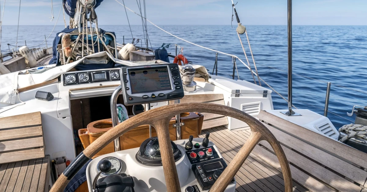 Sailboat helm and steering wheel overlooking the sea, representing recording a voyage at the helm.