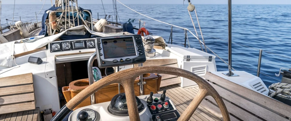 Sailboat helm and steering wheel overlooking the sea, representing recording a voyage at the helm.