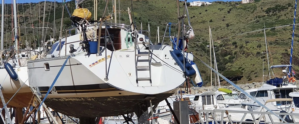 Sailboat resting on stands in a boatyard with a ladder against the hull, illustrating boat care and maintenance.