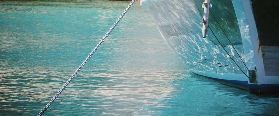 Anchor chain extending into clear turquoise water beside a boat at anchor.