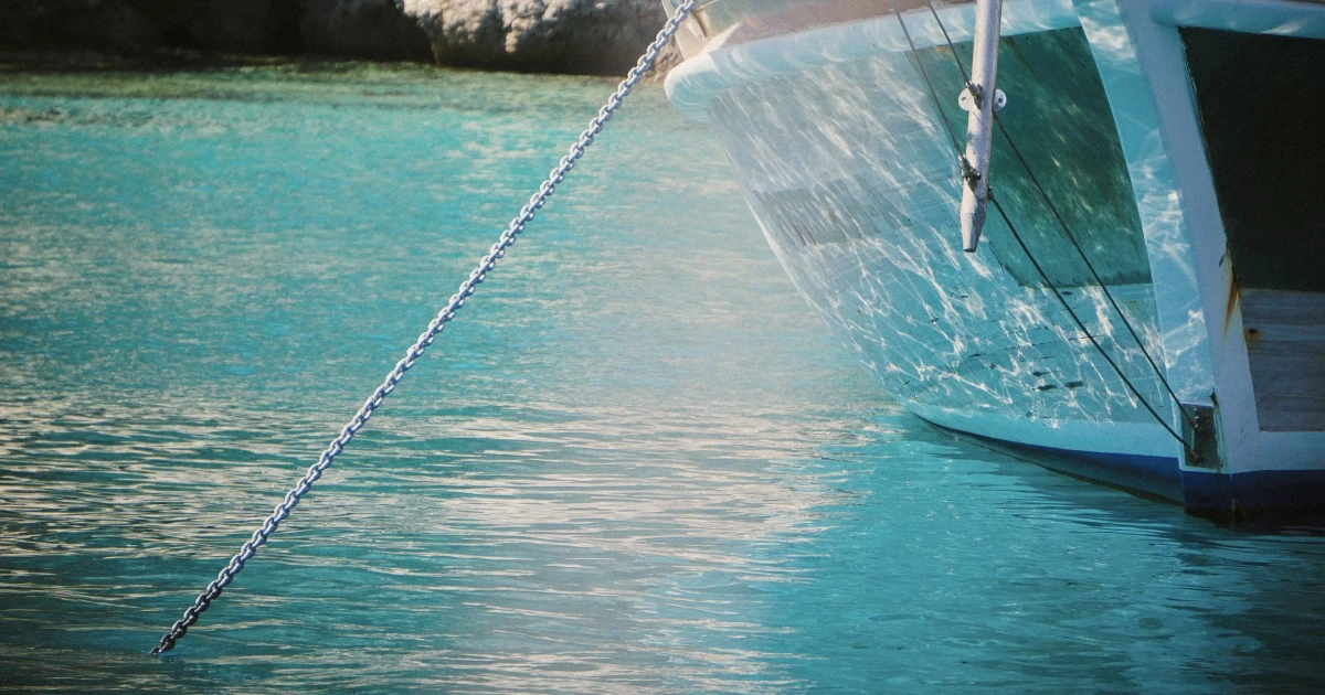Anchor chain extending into clear turquoise water beside a boat at anchor.