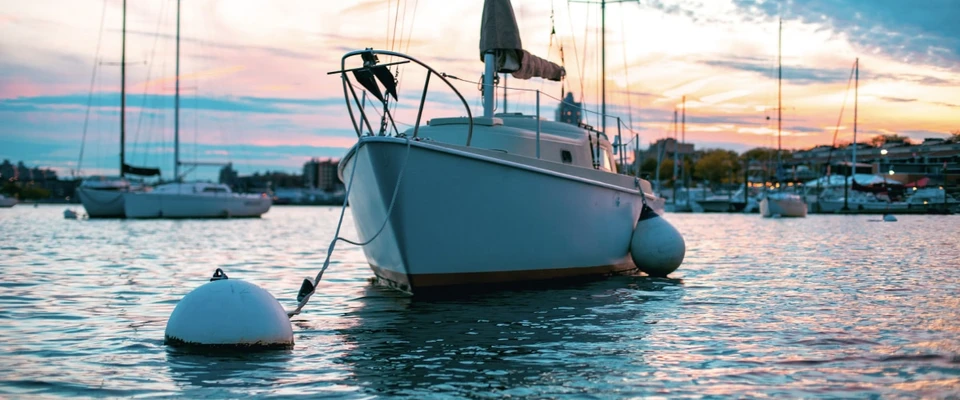 Sailboat secured to a mooring buoy in a calm harbour at sunset.