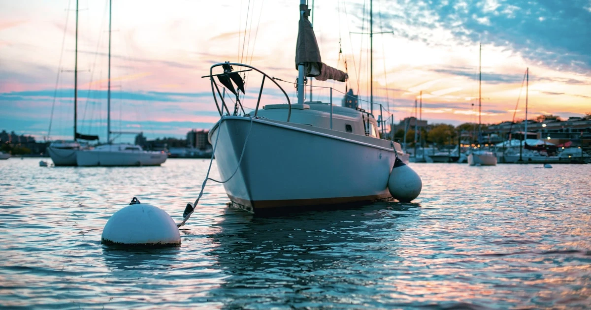 Sailboat secured to a mooring buoy in a calm harbour at sunset.