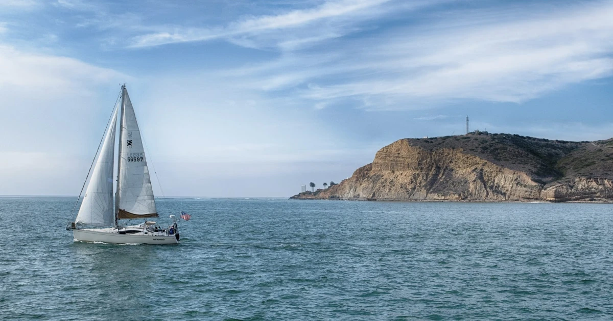 Aerial view of a sailboat underway, leaving a long wake across the open sea.