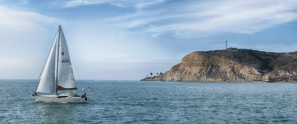 Aerial view of a sailboat underway, leaving a long wake across the open sea.