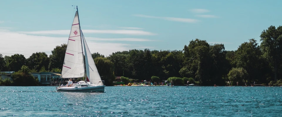 Sailboat cruising on calm blue water past a green coastline.