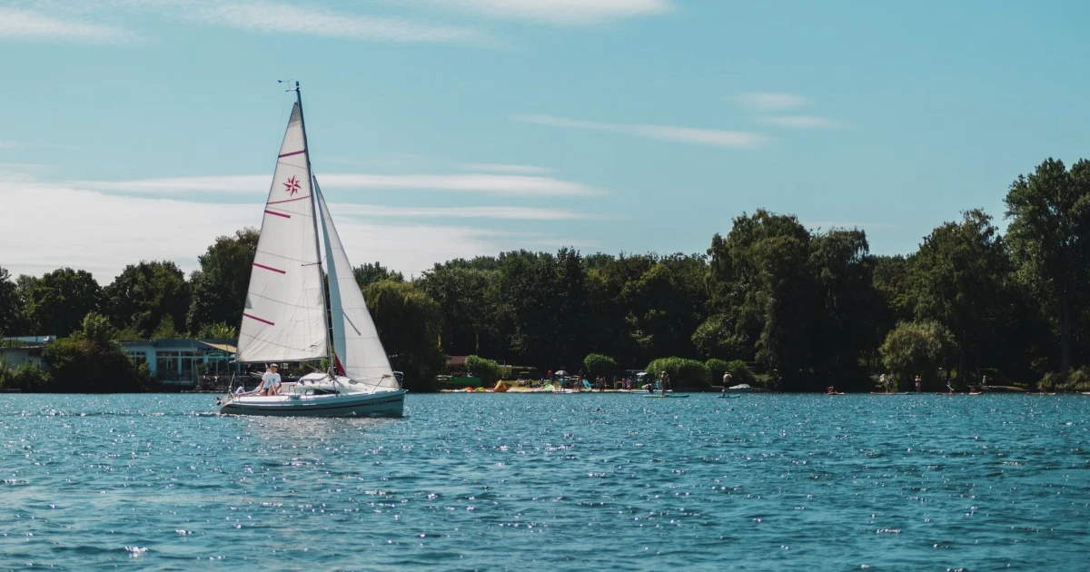 Sailboat gliding on calm turquoise water near a wooded shoreline