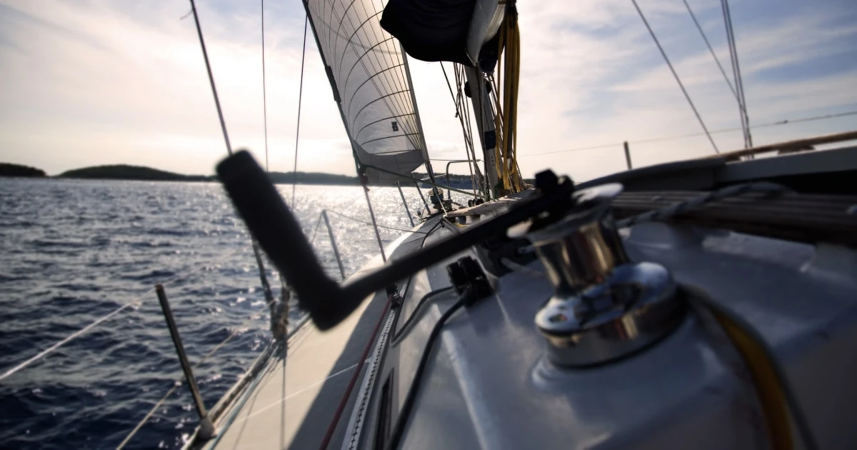 Winch and sail-handling gear on a sailboat deck at sunset.