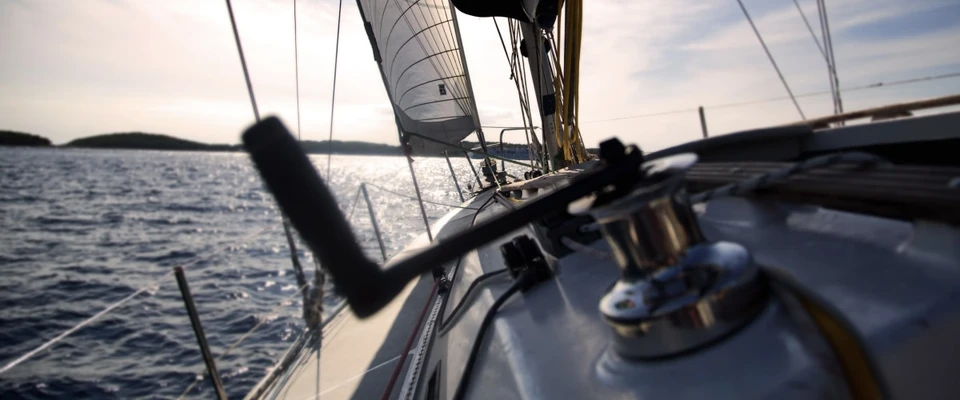 Winch and sail-handling gear on a sailboat deck at sunset.