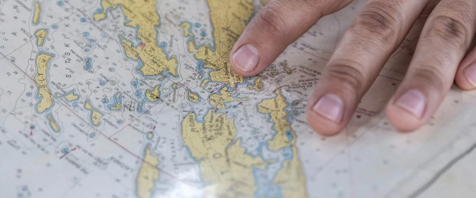 Hand resting on a paper nautical chart of a coastline.