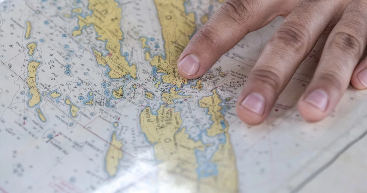Hand resting on a paper nautical chart of a coastline.