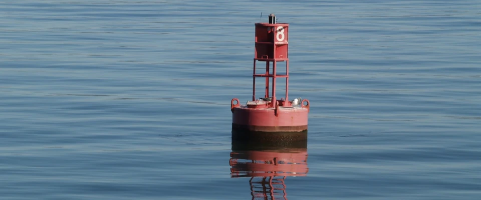 Red navigation buoy floating in calm water, illustrating the use of maritime channel markers.