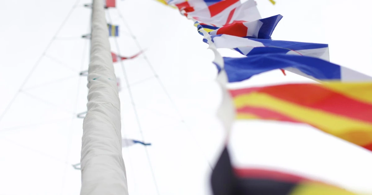 Colourful international maritime signal flags hanging from a sailboat's rigging.