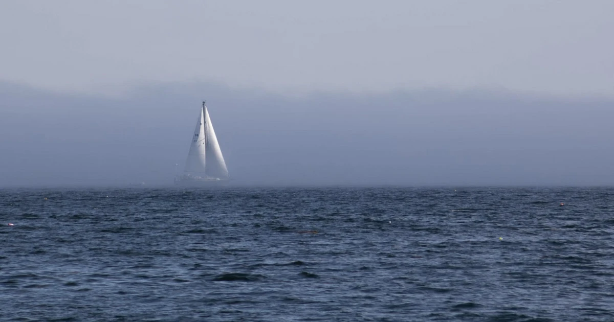 Sailboat on open water in hazy conditions with limited visibility.