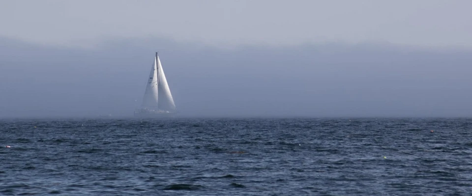 Sailboat on open water in hazy conditions with limited visibility.