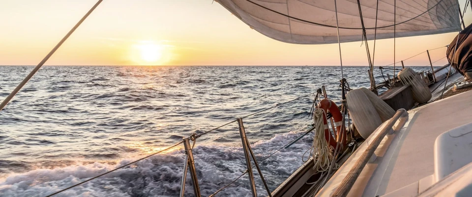Sailboat sailing across the sea at sunset, viewed from beneath its sail.