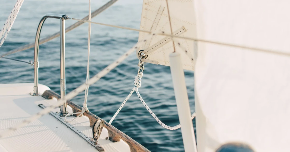 View along a sailboat's deck and rigging toward the clear blue sea.