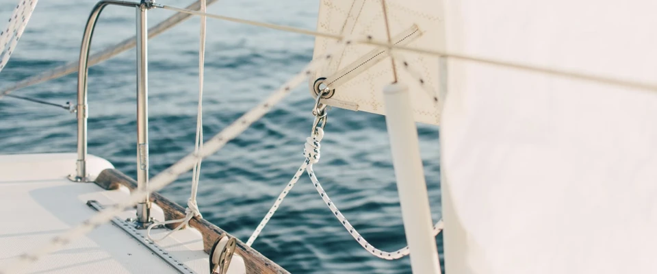 View along a sailboat's deck and rigging toward the clear blue sea.