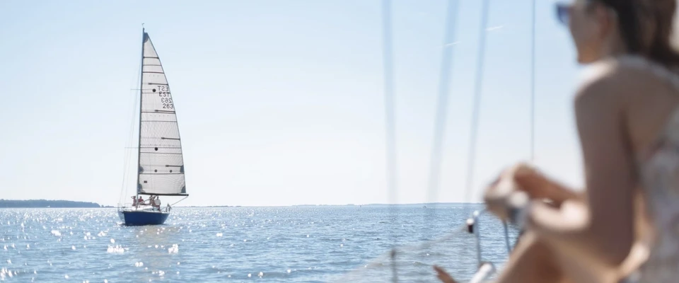 Sailboat on the horizon with a woman sitting on deck in the foreground.