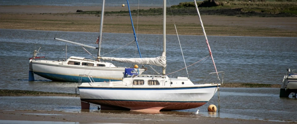 Sailboat resting in shallow water near the shore at low tide.