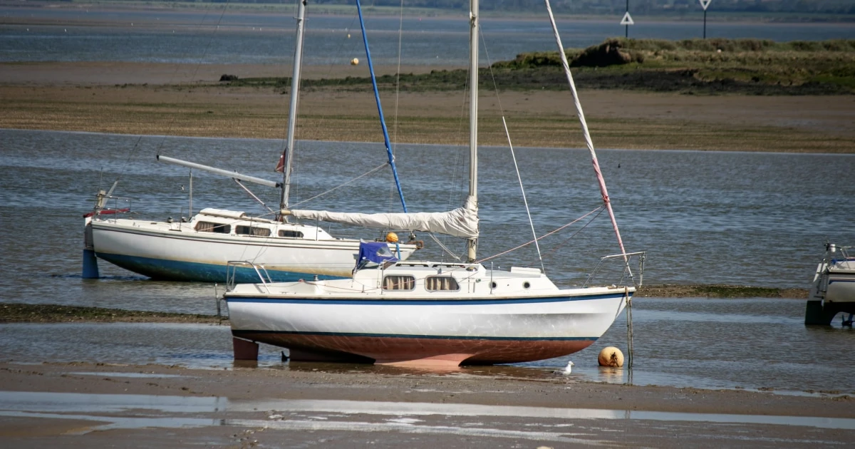 Sailboat resting in shallow water near the shore at low tide.
