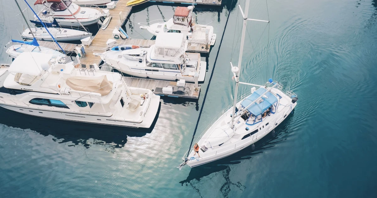 Aerial view of sailboats and motorboats in a turquoise marina.