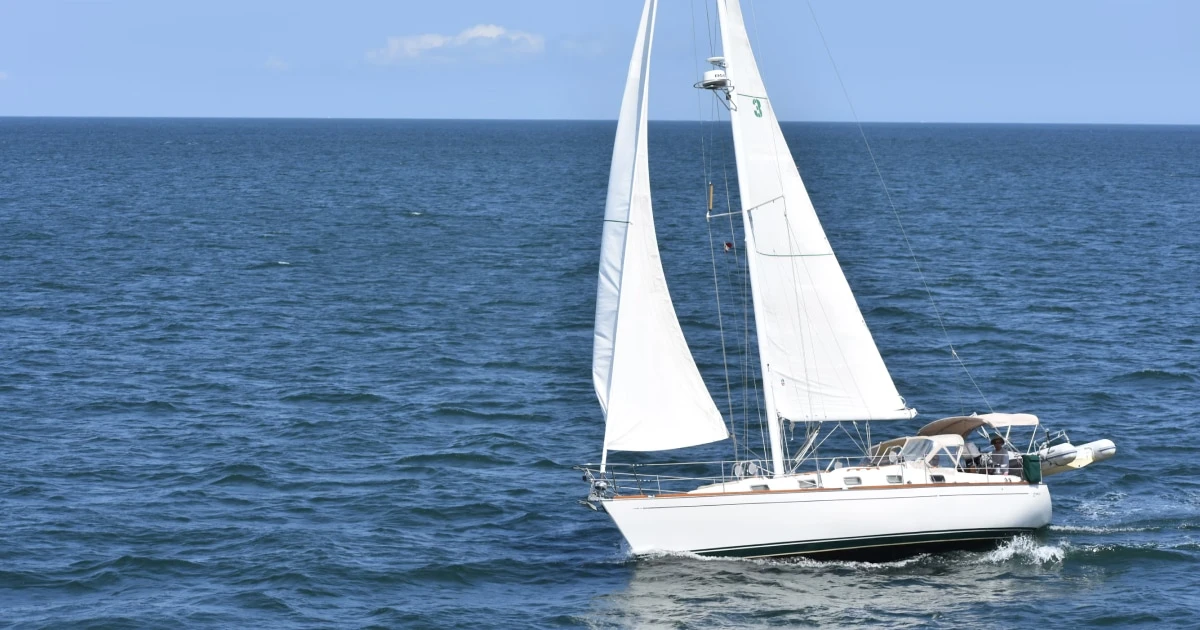 Sailboat sailing across blue water with its white sails raised.