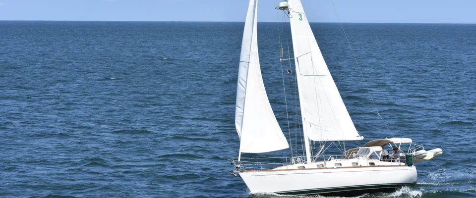 Sailboat sailing across blue water with its white sails raised.