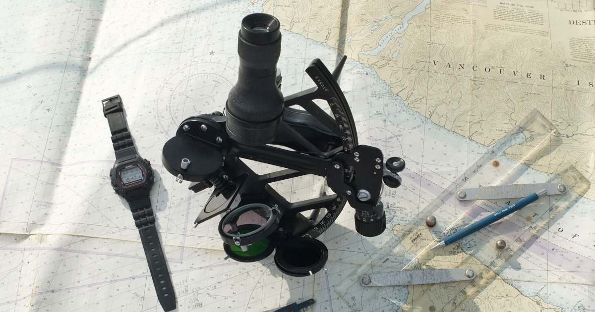 Sextant and wristwatch resting on a nautical chart with plotting tools.