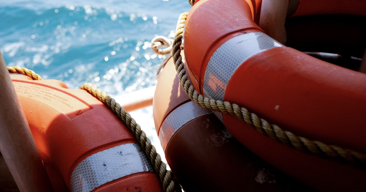 Orange lifebuoy with reflective bands on a boat, sea in the background.
