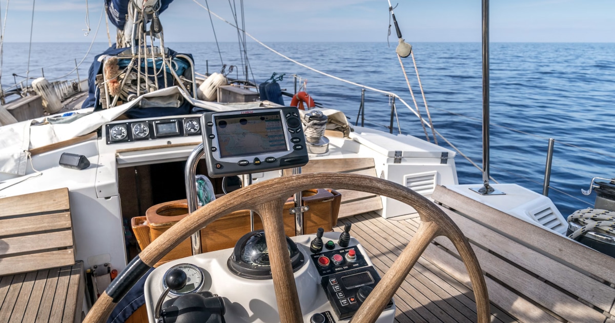 Sailboat helm and steering wheel overlooking the sea, representing recording a voyage at the helm.