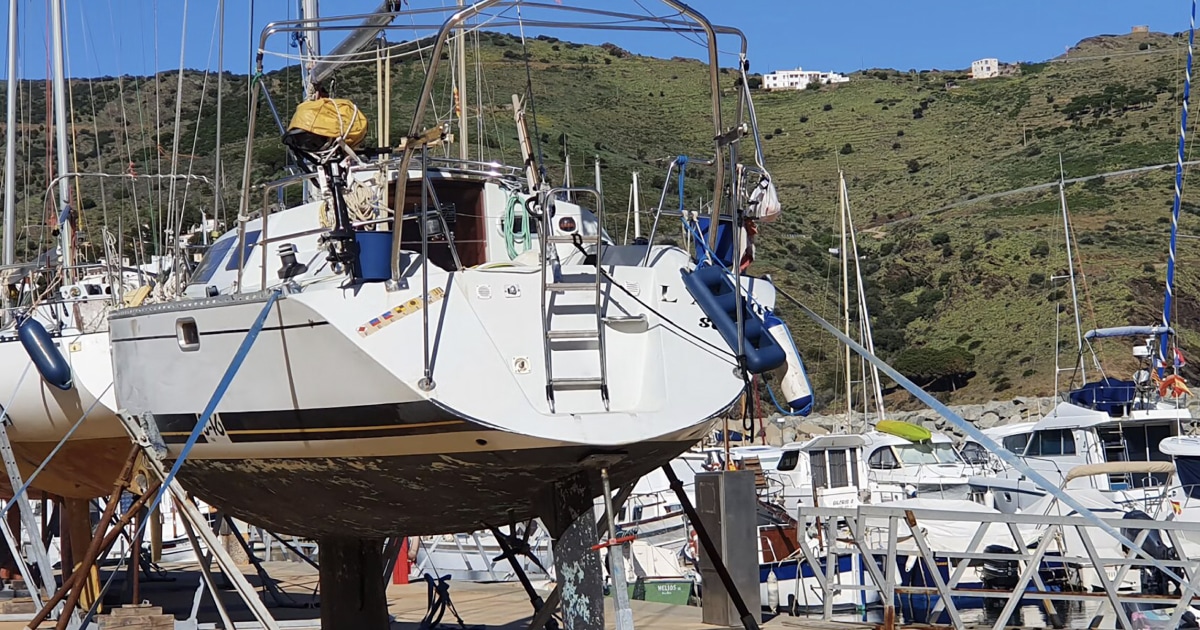 Sailboat resting on stands in a boatyard with a ladder against the hull, illustrating boat care and maintenance.
