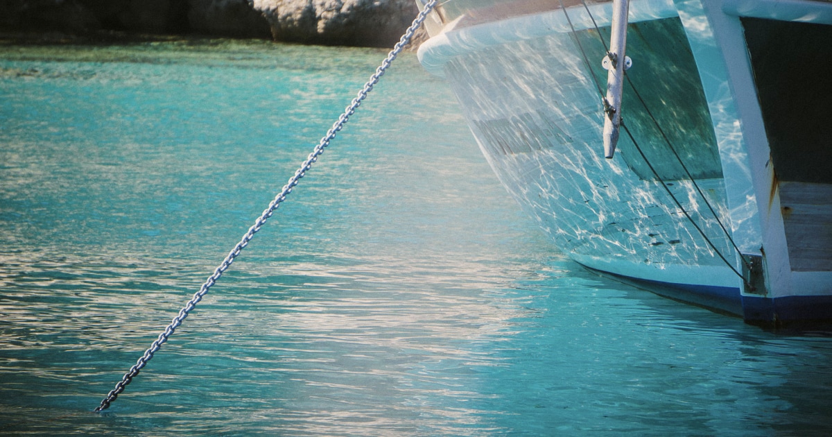 Anchor chain extending into clear turquoise water beside a boat at anchor.