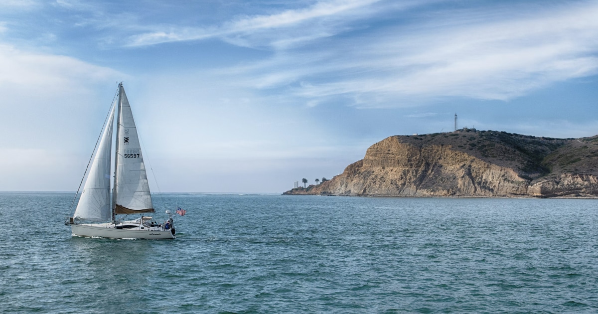 Aerial view of a sailboat underway, leaving a long wake across the open sea.