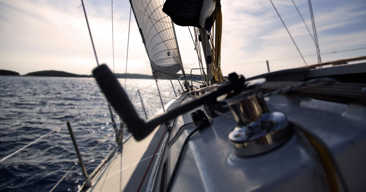 Winch and sail-handling gear on a sailboat deck at sunset.