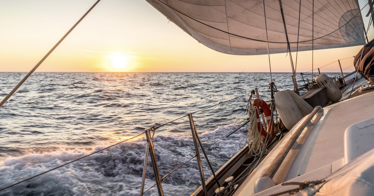 Sailboat sailing across the sea at sunset, viewed from beneath its sail.