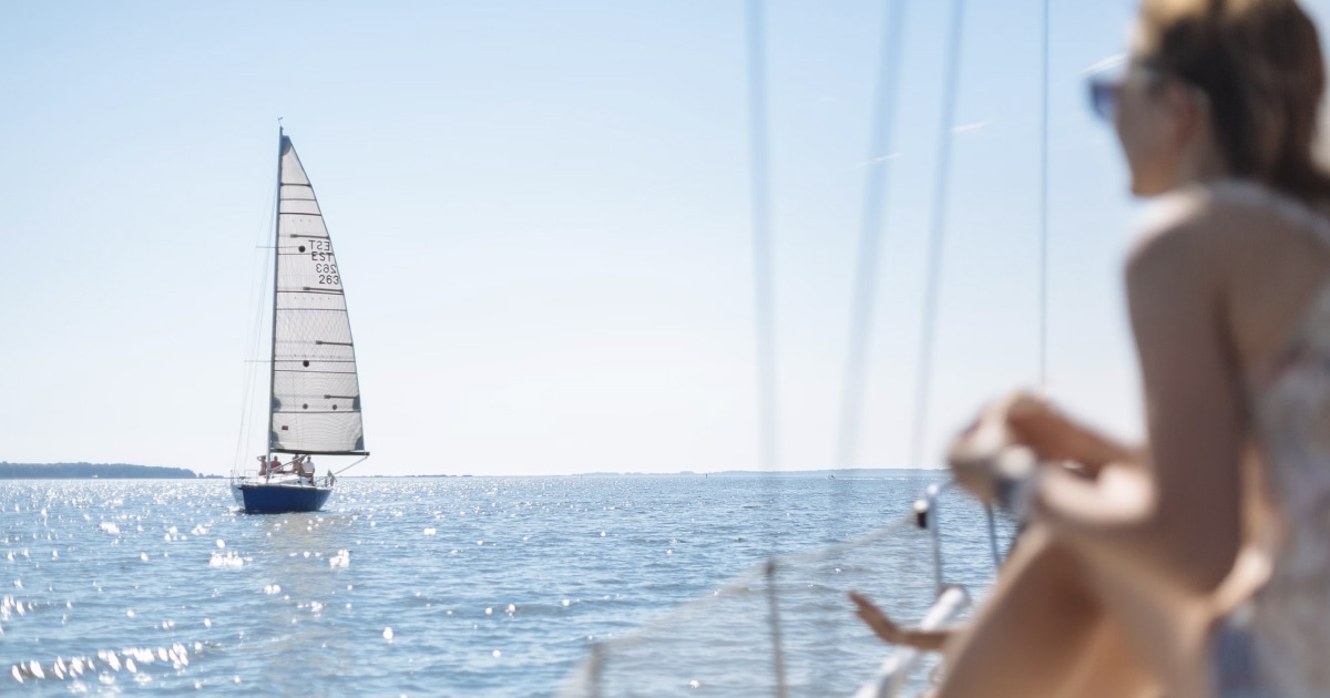 Sailboat on the horizon with a woman sitting on deck in the foreground.