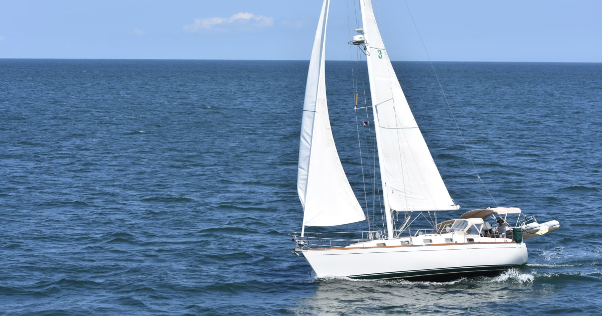 Sailboat sailing across blue water with its white sails raised.